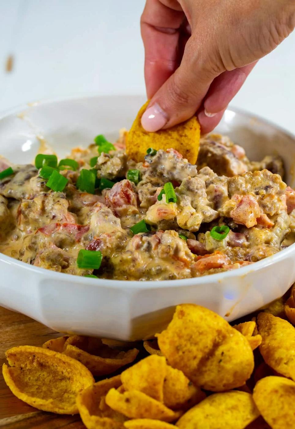 Hand sticking frito chip into dip.