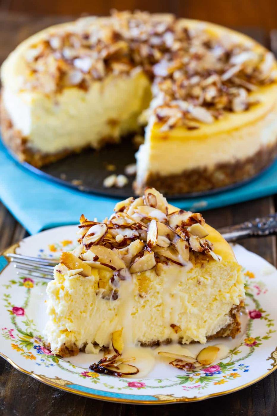 Slice of cheesecake on plate with rest of cheesecake in background.