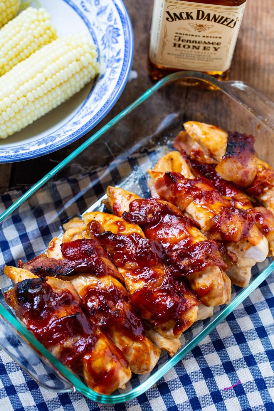 Cooked BBQ Chicken in a 9x13-inch baking dish, bowl of corn, and bottle of bourbon.