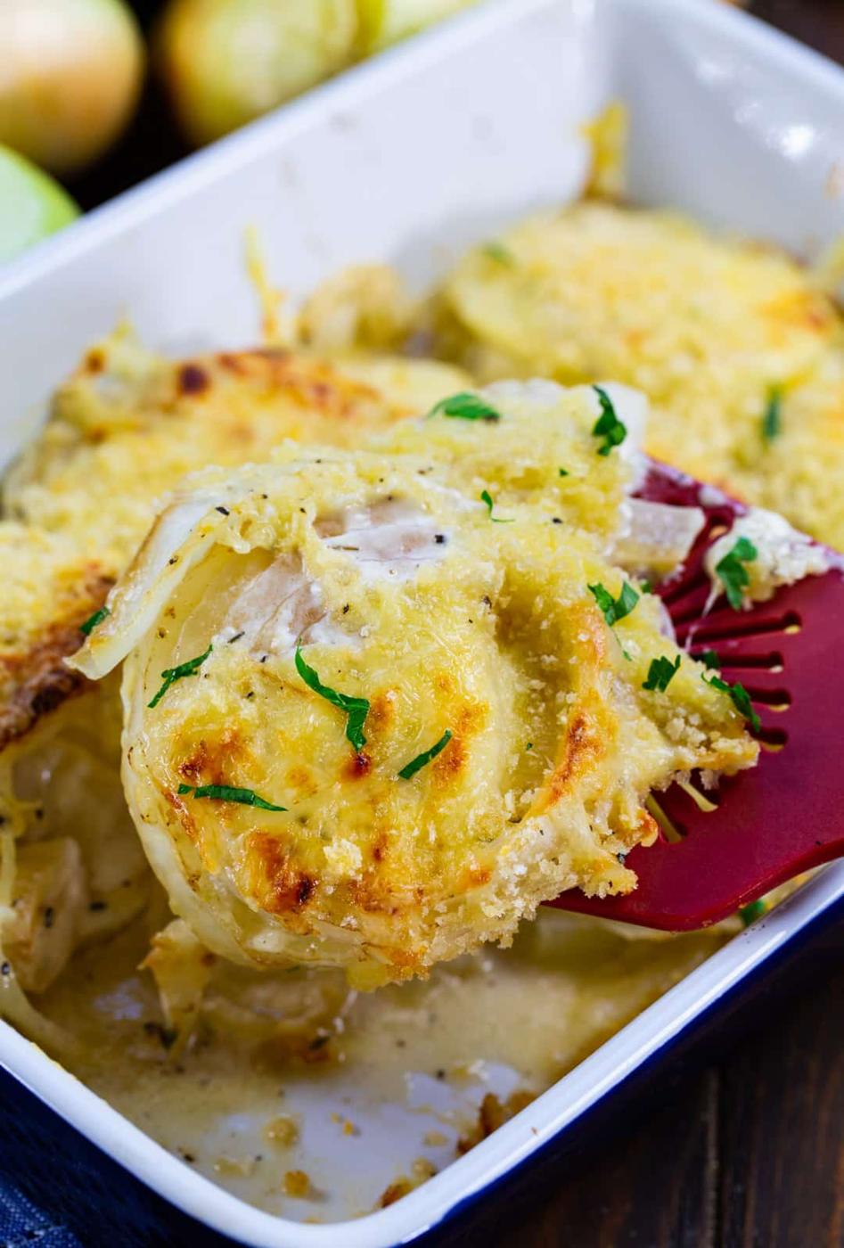 Spatula lifting Vidalia onions out of baking dish.