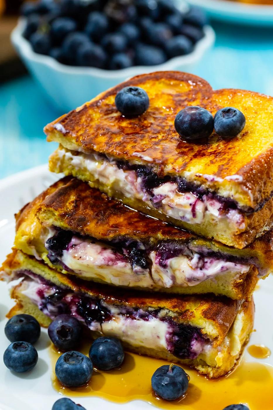 Blueberry Stuffed French Toast halves stacked up on a plate and drizzled with maple syrup.