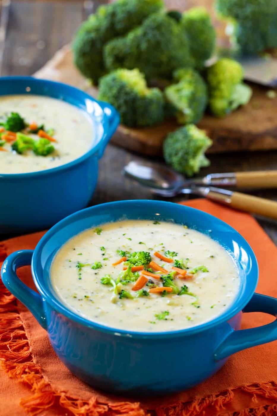 Broccoli soup in a bowl and fresh broccoli in background.