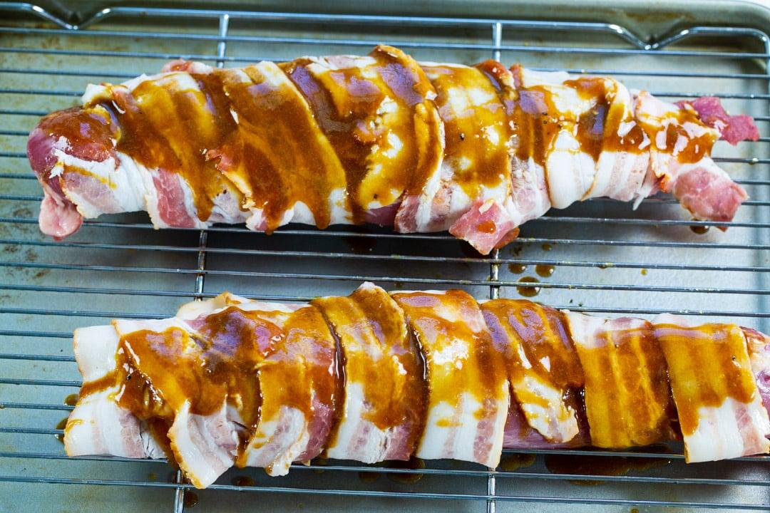 Uncooked pork tenderloins wrapped in bacon.
