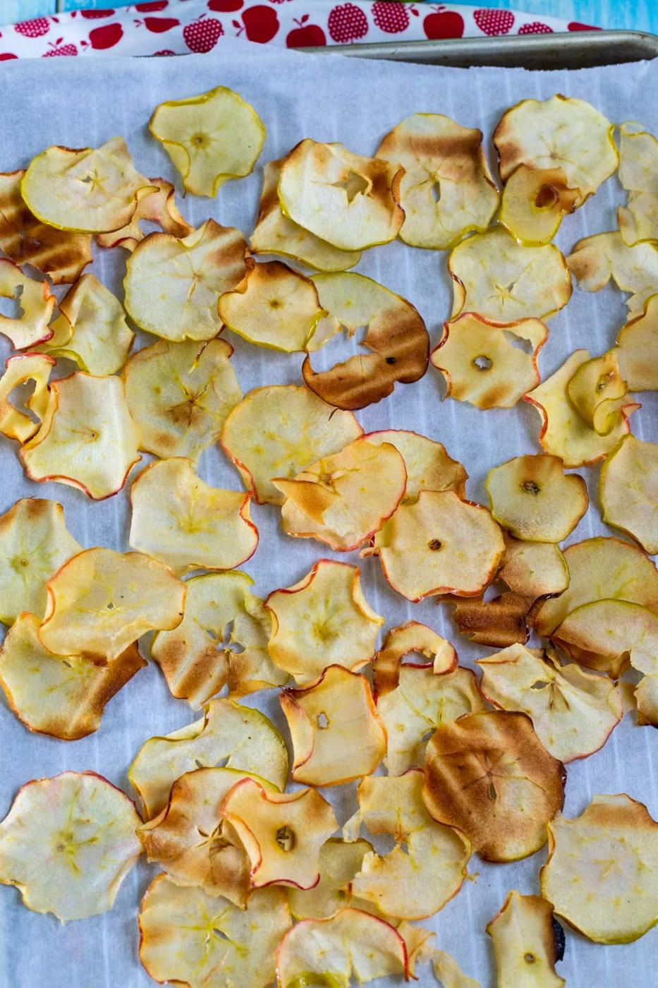 Cooked Apple chips on parchment paper-lined baking sheet.