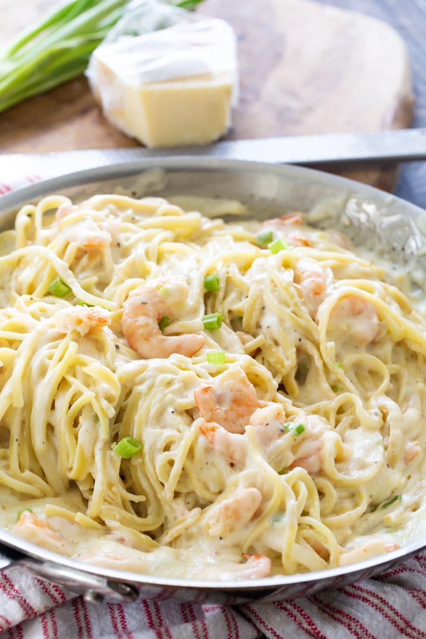 Pan full of Shrimp Alfredo with Parmesan cheese in background