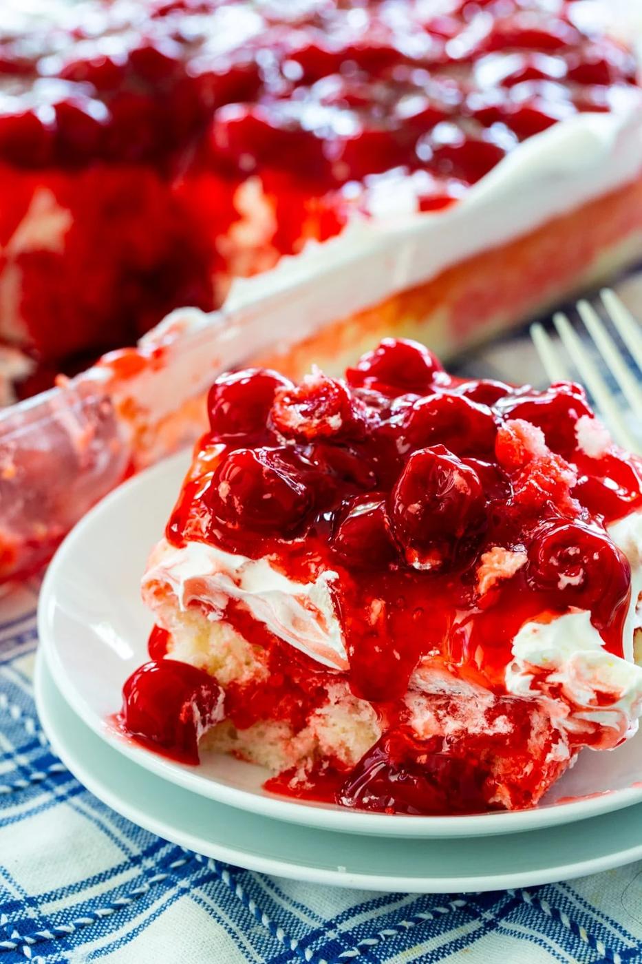 Slice of Poke Cake with cherries on a plate.