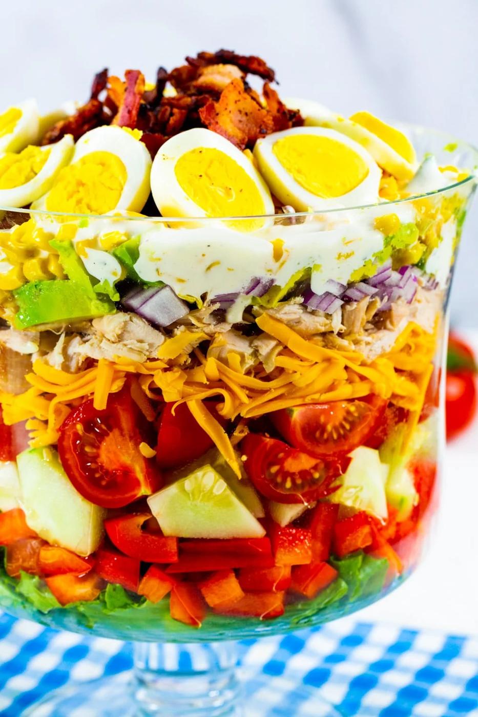 Layer Salad topped with hard-boiled egg and bacon in a trifle dish.
