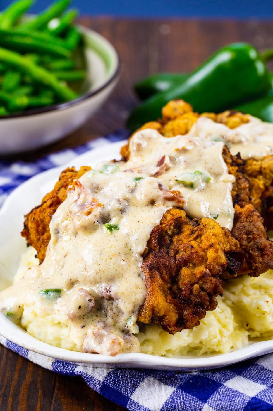 Chicken Fried Steak on a serving platter with bowl of green beans in background.