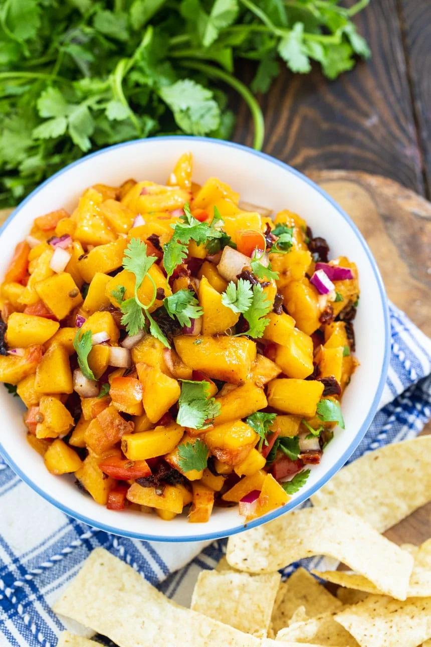 Chipotle Peach Salsa in a bowl surrounded by tortilla chips and fresh cilantro.