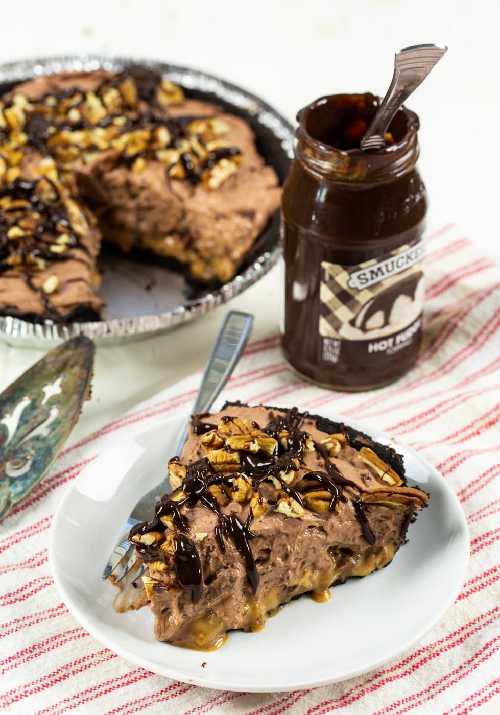 Slice of pie on a plate with rest of pie and jar of fudge sauce in background.