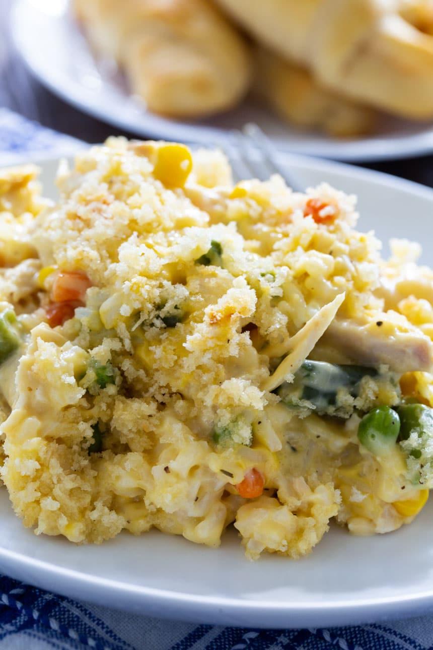 Creamy Chicken and Rice Casserole on a white plate with crescent rolls in background.
