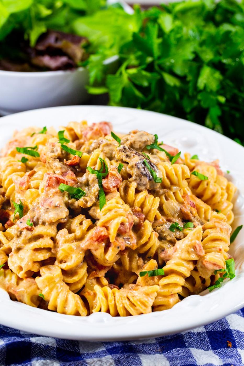 Creamy Pasta wit Rotel Tomatoes and Sausage in a white bowl with parsley in background.