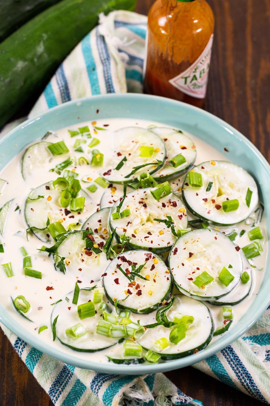 Creamy Cucumbers in a bowl and a bottle of hot sauce.