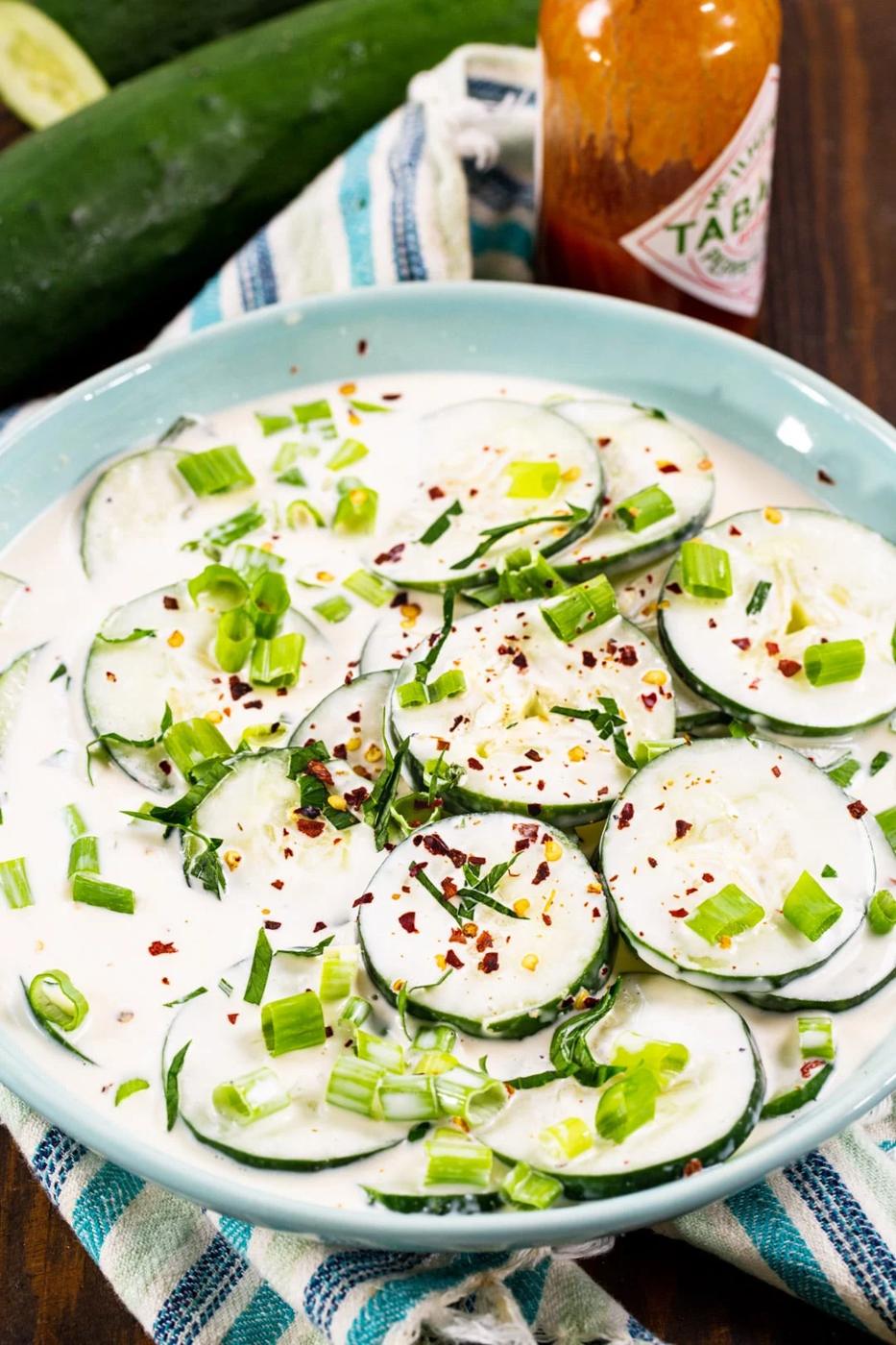 Creamy Spicy Cucumbers in blue bowl and bottle of hot sauce.