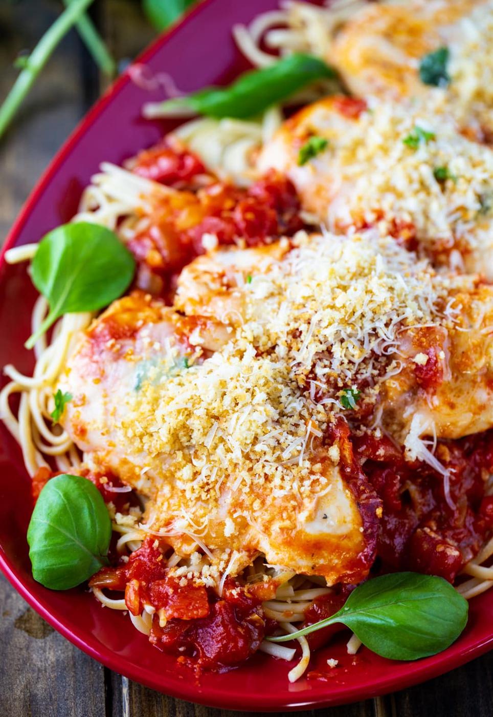 Chicken over pasta on a plate with fresh basil.