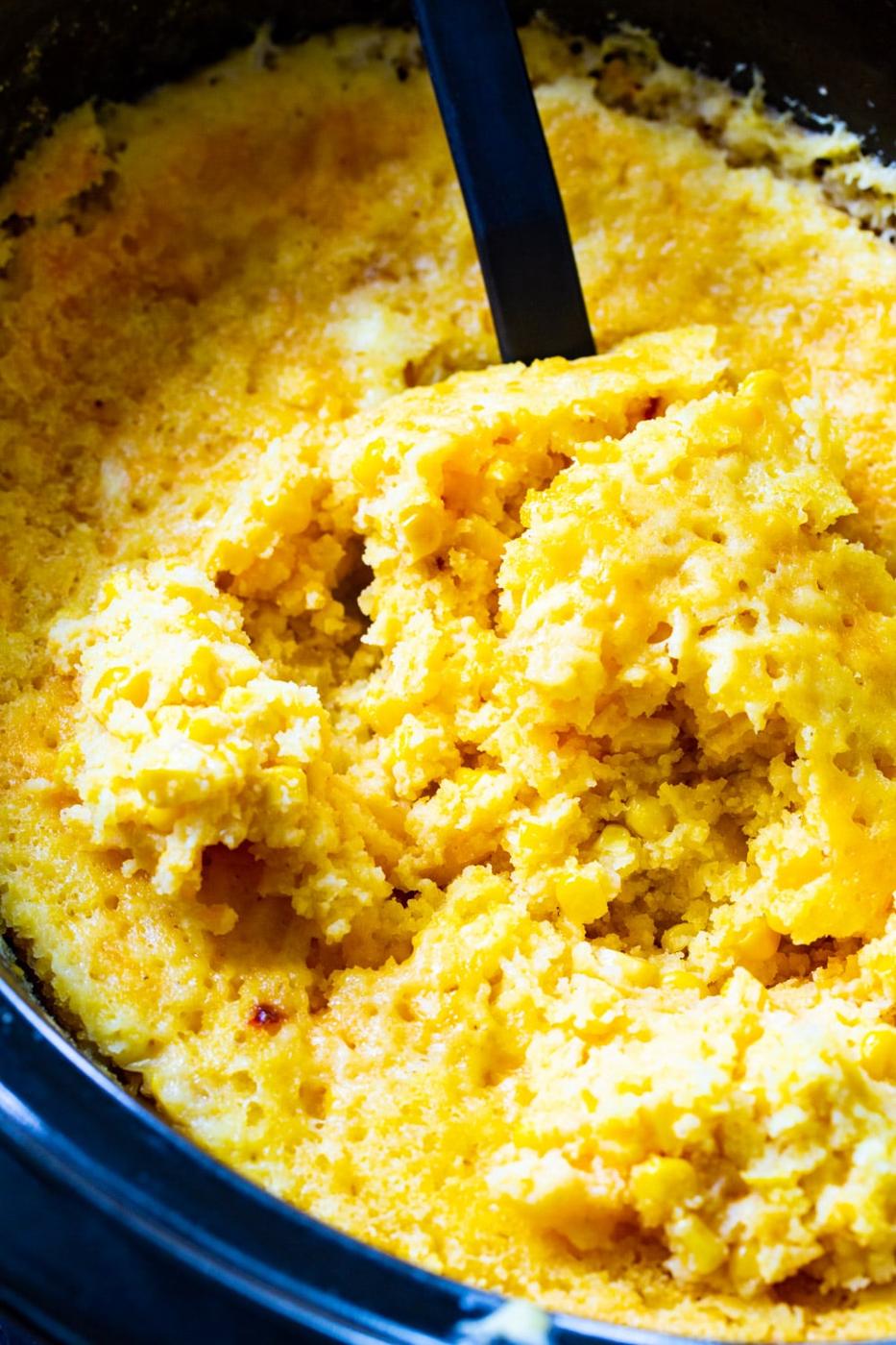 Spoon scooping corn casserole in slow cooker.