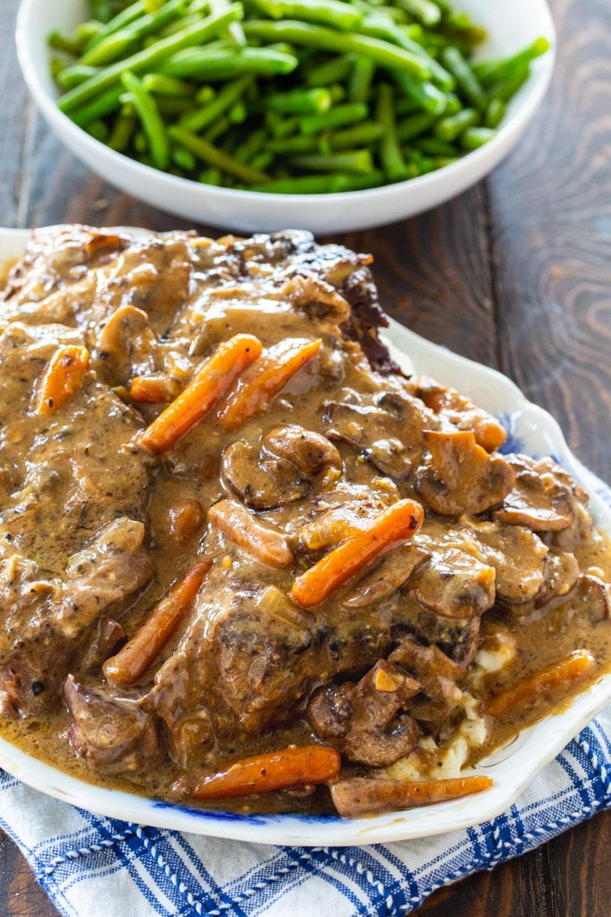 Crock Pot Roast with Creamy Mushroom Gravy on serving platter with bowl of peas.