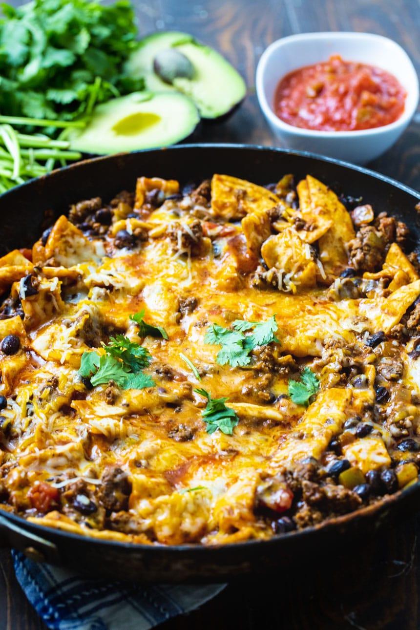 Burrito Skillet in a alrge skillet with avocado and cilantro in background.