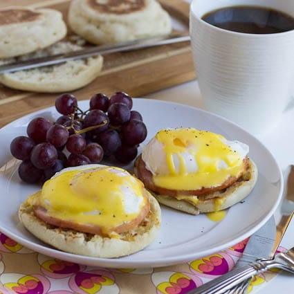 Eggs Benedict on a plate with red grapes with a cup of coffee.