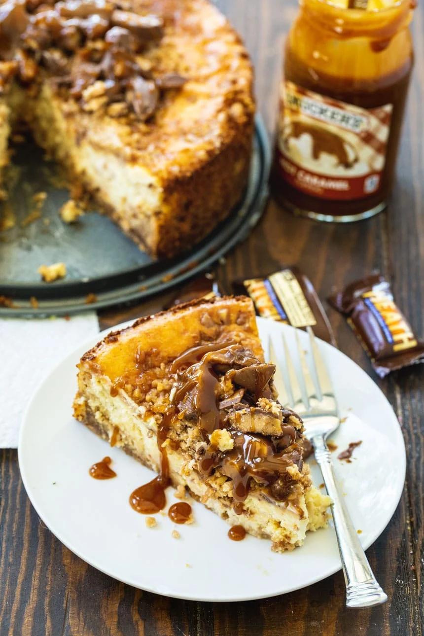A slice of Toffe Cheesceake with a jar of caramel sauce in background.