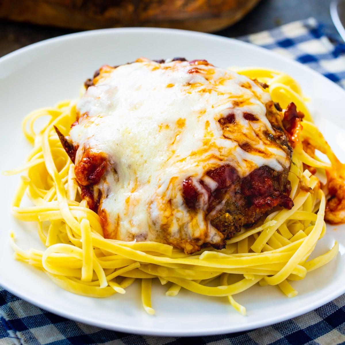 Italian Cubed Beef over spaghetti on a white plate.