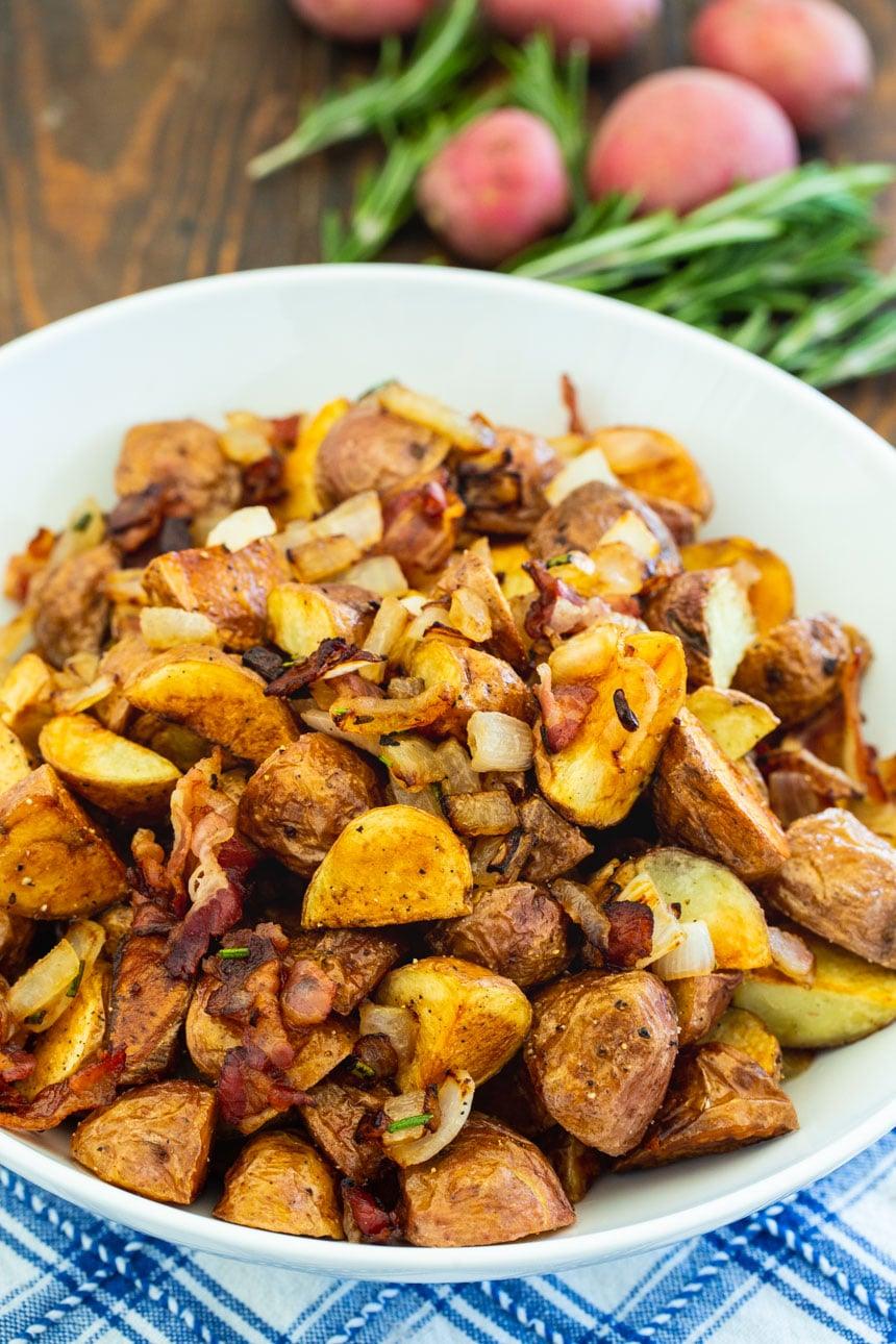 Italian Roasted Potatoes in white bowl with red potatoes and rosemary in background