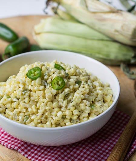 Jalapeno Creamed Corn in serving bowl with corn on the cob in background.