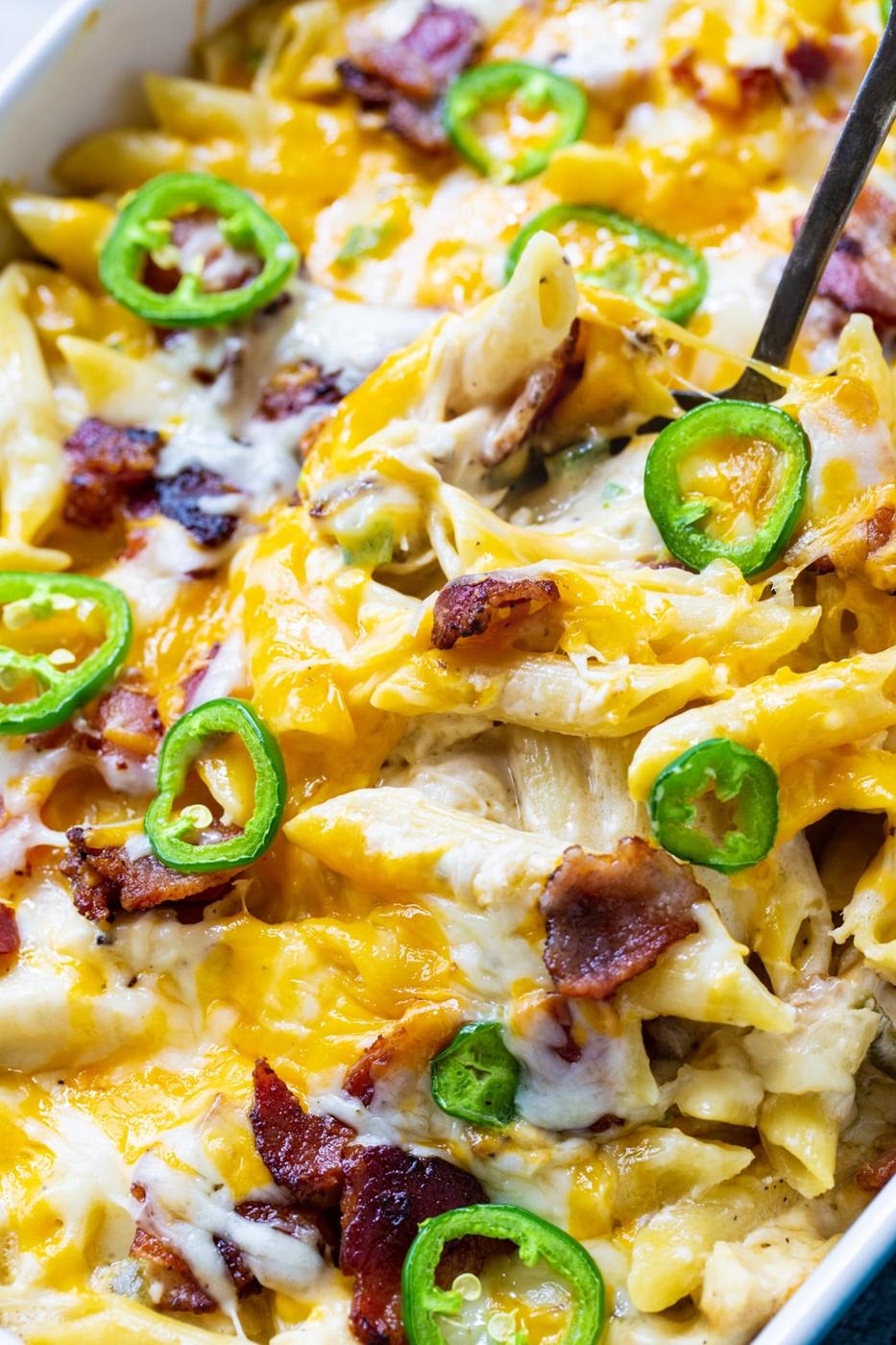 Spoon scooping up Chicken Casserole topped with jalapenos in baking dish.