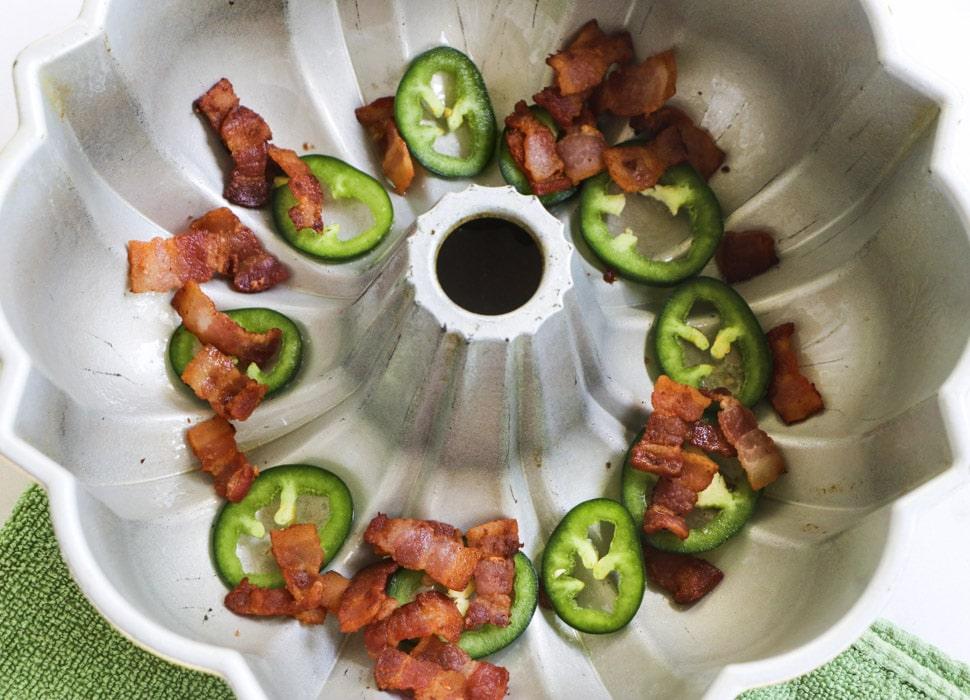Bacon pieces and jalapeno slices in bottom of bundt pan.