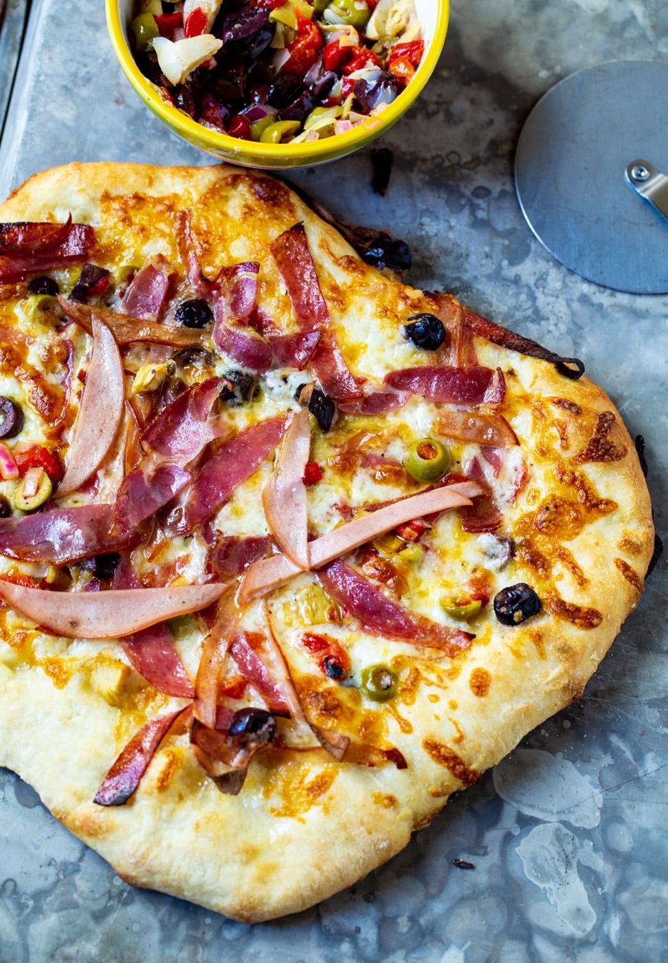 Whole pizza and a bowl of olive salad.