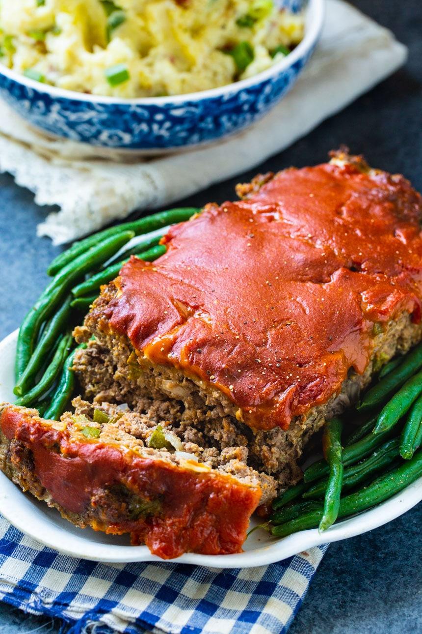 Meatloaf on plate with green beans and mashed potatoes in background.