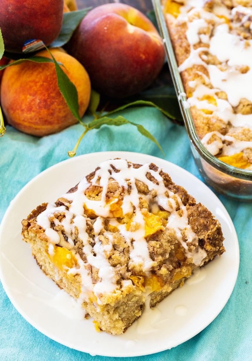 Peach Crisp Coffee Cake slice on a plate with peaches in background