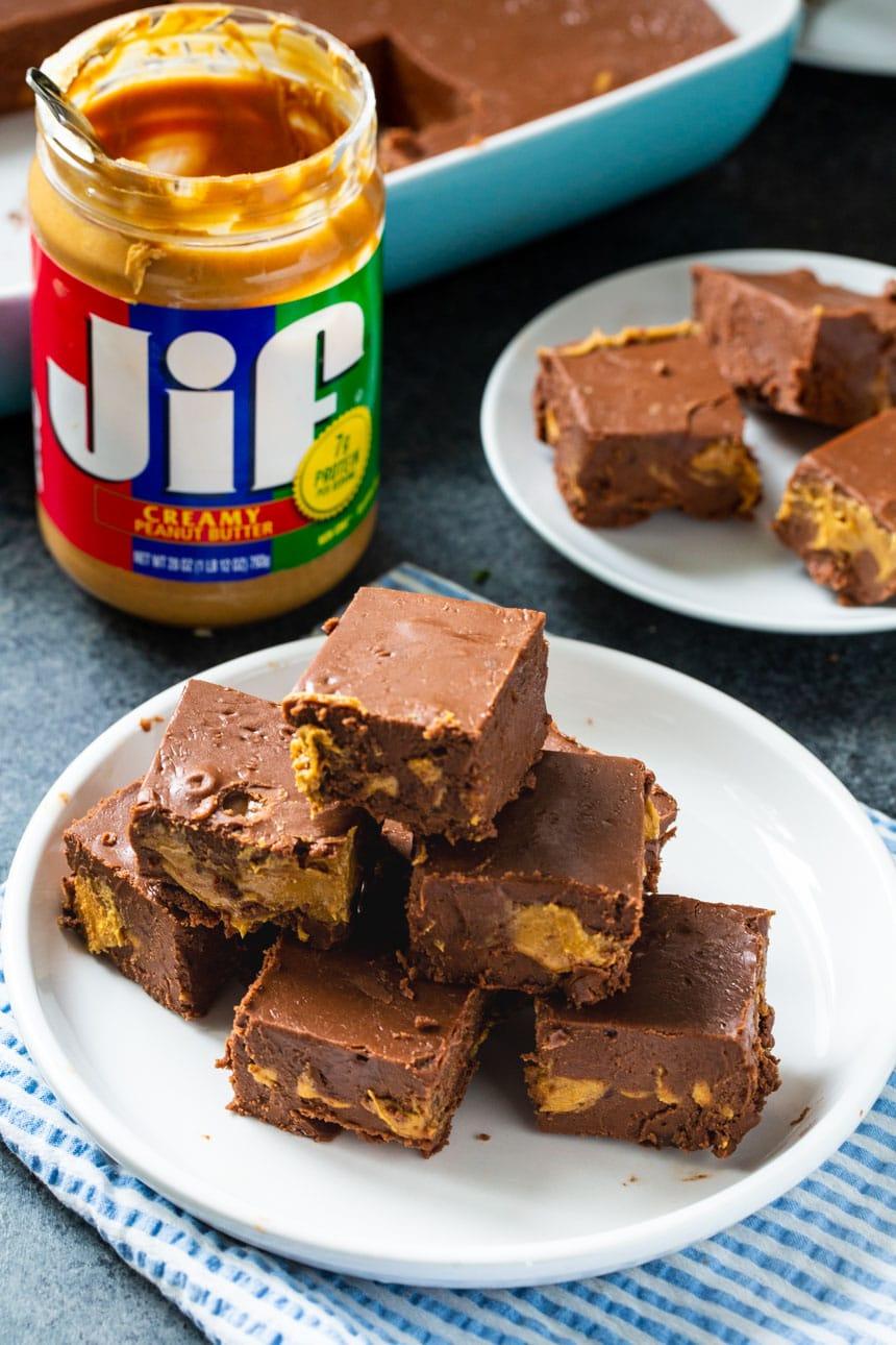 Squares of fudge on a plate with jar of peanut butter in background.