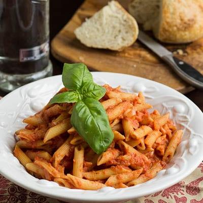 Pasta in a white bowl with bread in the background.
