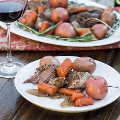 Single serving of Pot Roast on a white plate with a glass of red wine.