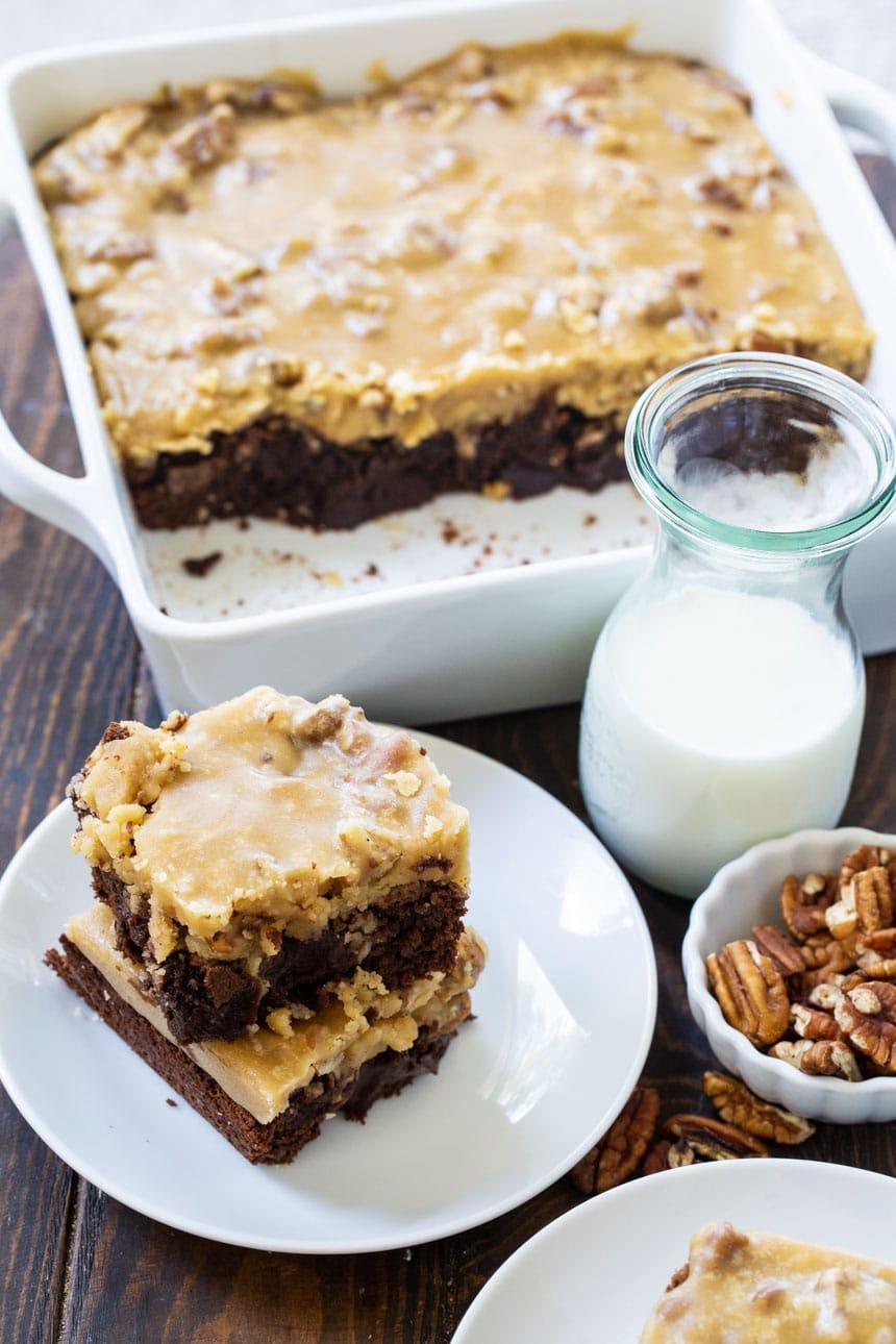 two brownies on a plate with jug of milk and pan full of brownies in background.