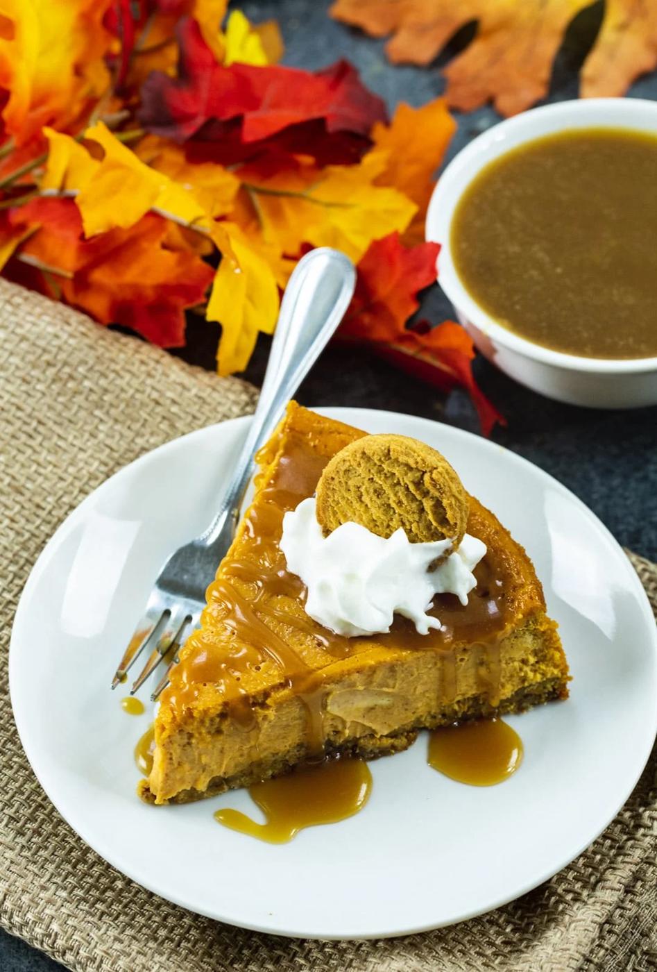 Pumpkin Cheesecake with Gingersnap Crust on a plate, plus fall leaves and a bowl of caramel sauce.