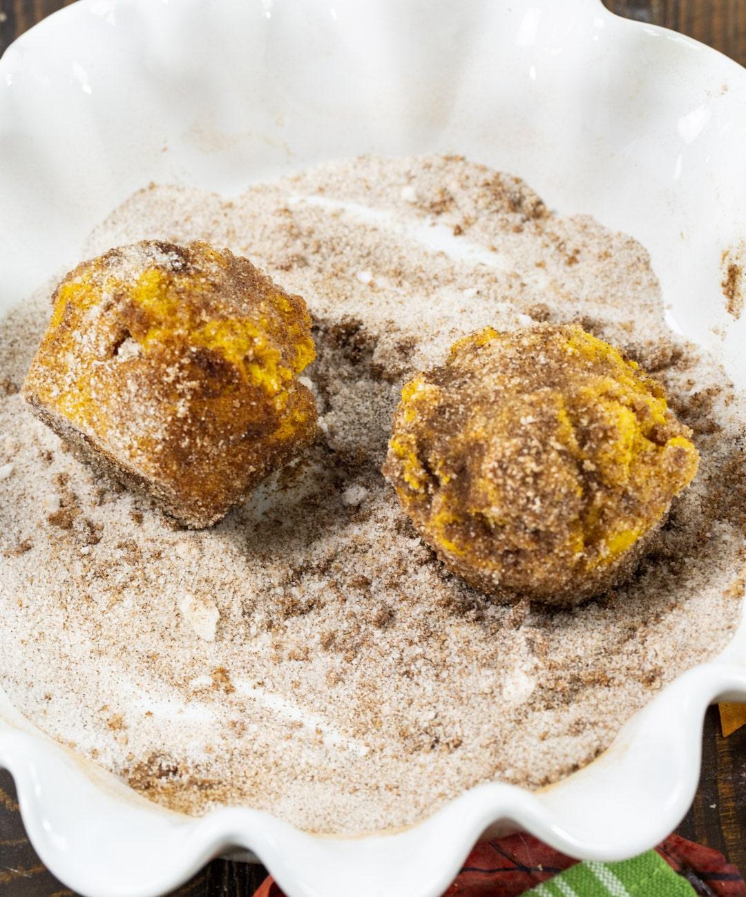Muffins getting coated in cinnamon sugar.
