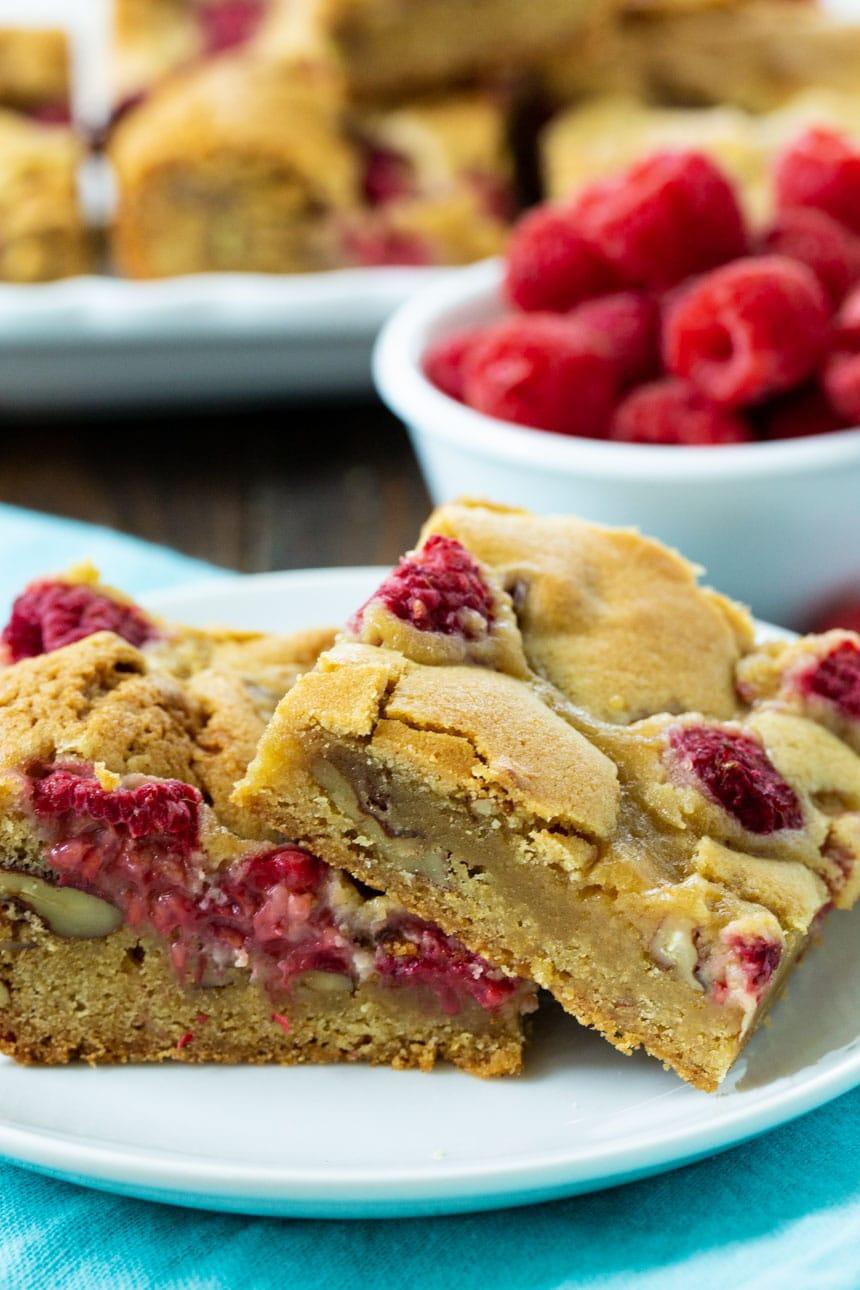 Raspberry Pecan Blondies on a plate with more blondies and raspberries in background.