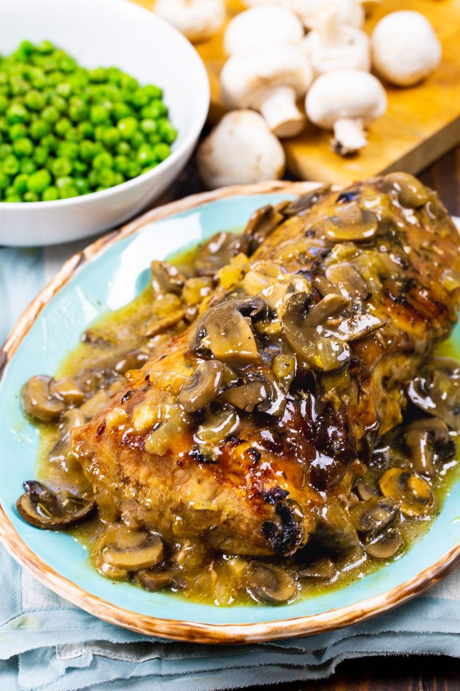 Roasted Pork Loin with Mushroom Gravy on serving platter with bowl of peas.