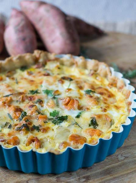 Roasted Sweet Potato Quiche in blue tart pan with sweet potatoes in background.