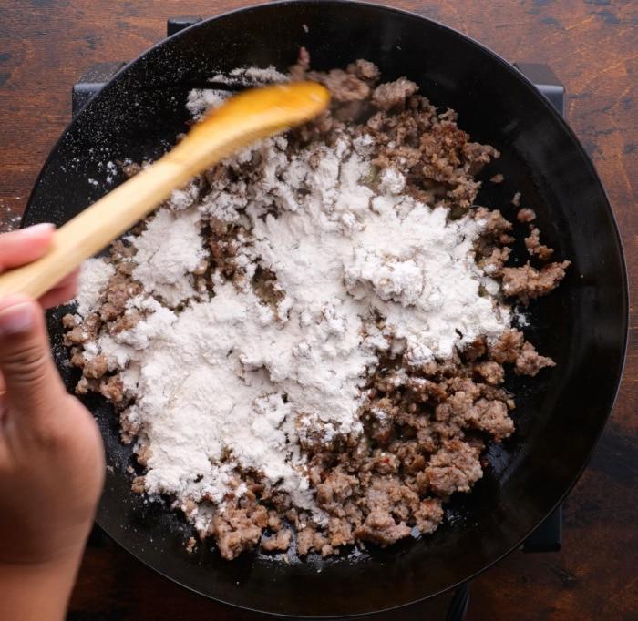 Sprinkling flour over sausage.