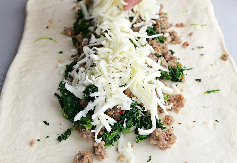 Sprinkling cheese over sausage.