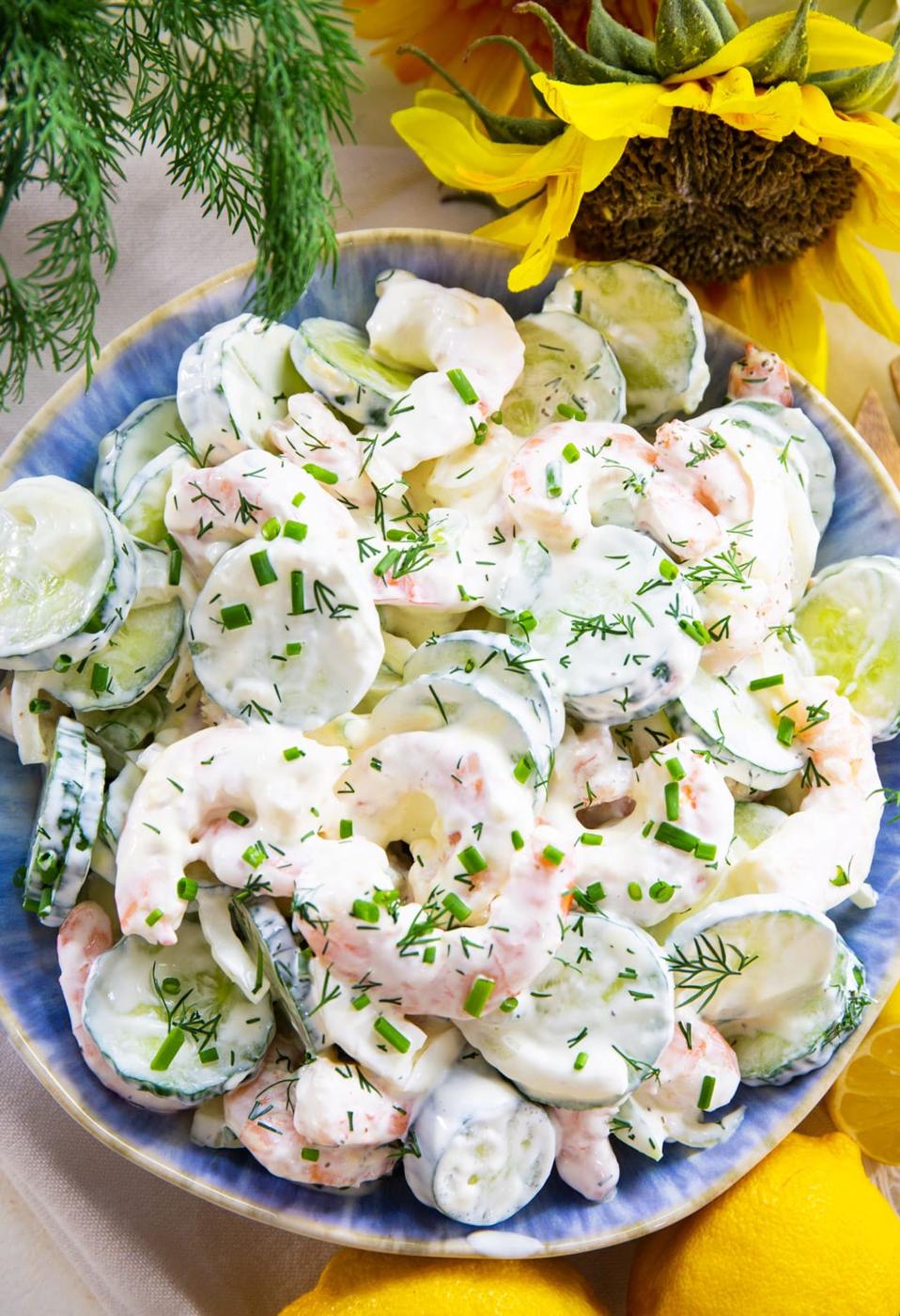 Shrimp Cucumber Salad in a blue serving bowl surrounded by lemons and flowers.
