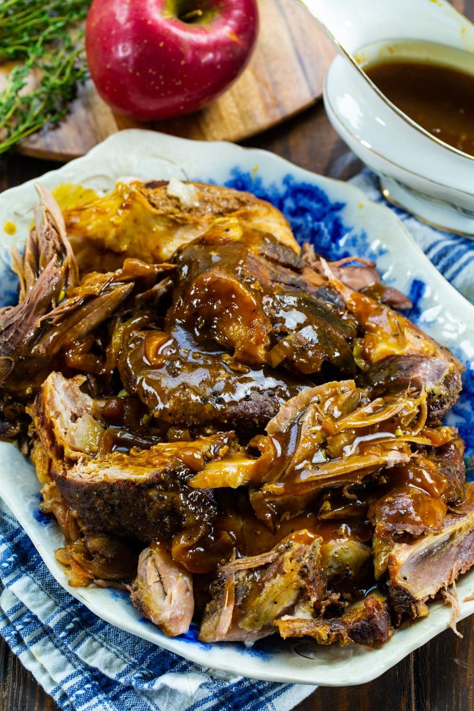 Apple Cider Pork pulled into pieces with apple and gravy in background.