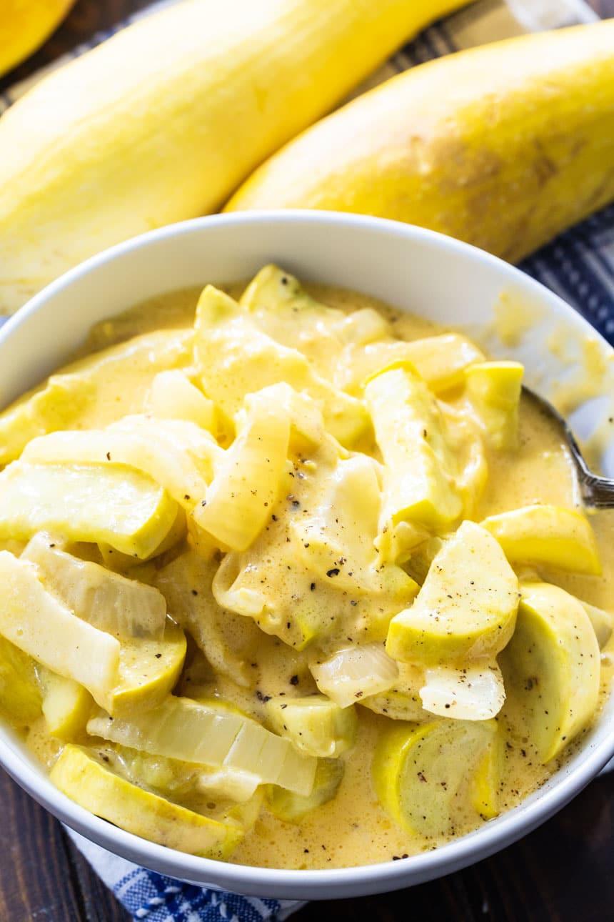 Cheesy Yellow Squash in a white bowl with squash in the background