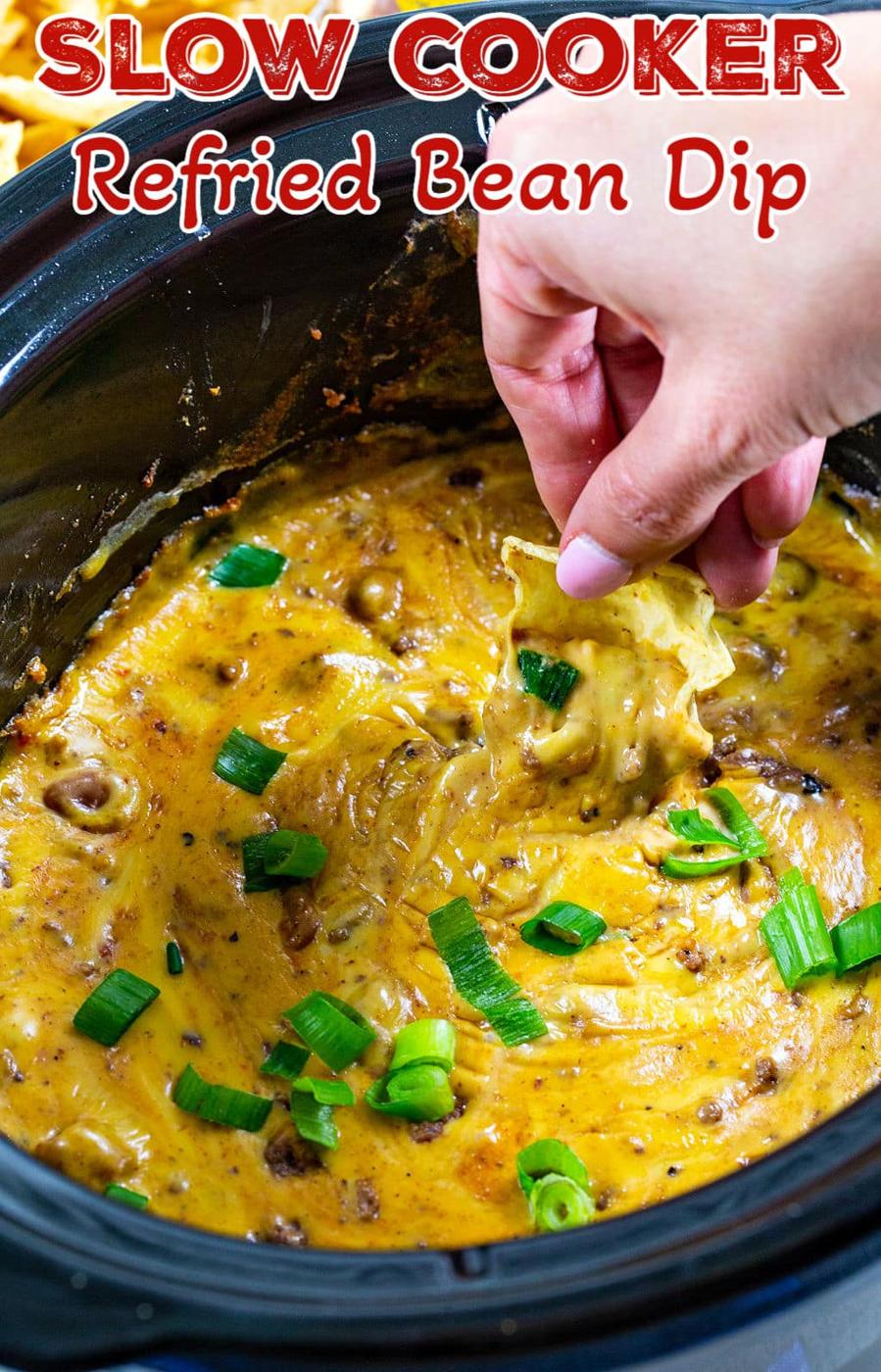 Chip scooping up Refried Bean Dip out of slow cooker.