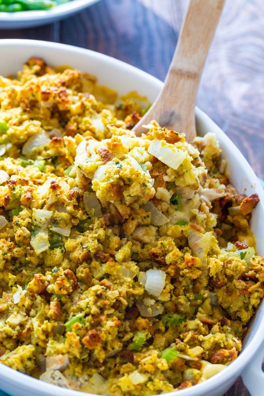 Wooden spoon scooping chicken stuffing casserole out of baking dish.