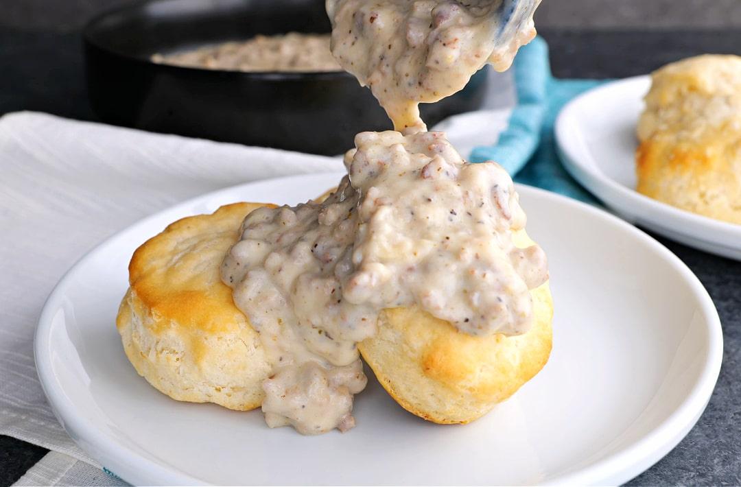 Sausage gravy being spooned over biscuits.