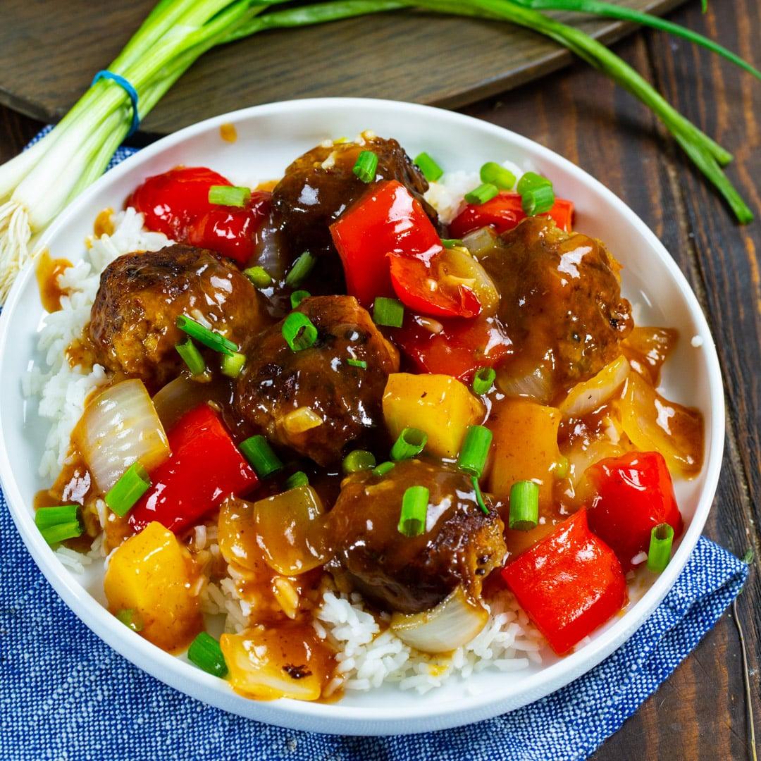 Meatballs over white rice on a plate.